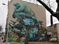 Co to jest mural? Ogromna, surrealistyczna grafika na ścianie budynku, przedstawiająca myślącą postać, krajobraz morski, jedzenie i przedmioty codziennego użytku.