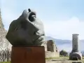 Kamienna rzeźba głowy z pęknięciami na tle ruin i gór.