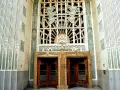 Monumentalne drzwi i okno w stylu art deco, ozdobione geometrycznymi wzorami i stylizowanymi motywami.