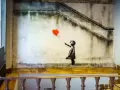 Banksy dziewczynka z balonikiem, unoszącym się na tle schodów i zniszczonej ściany.