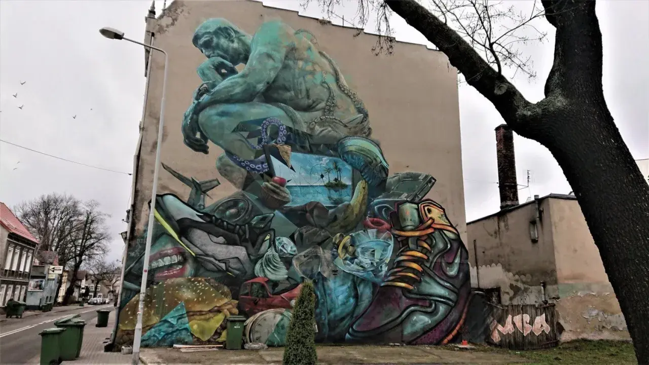 Co to jest mural? Ogromna, surrealistyczna grafika na ścianie budynku, przedstawiająca myślącą postać, krajobraz morski, jedzenie i przedmioty codziennego użytku.