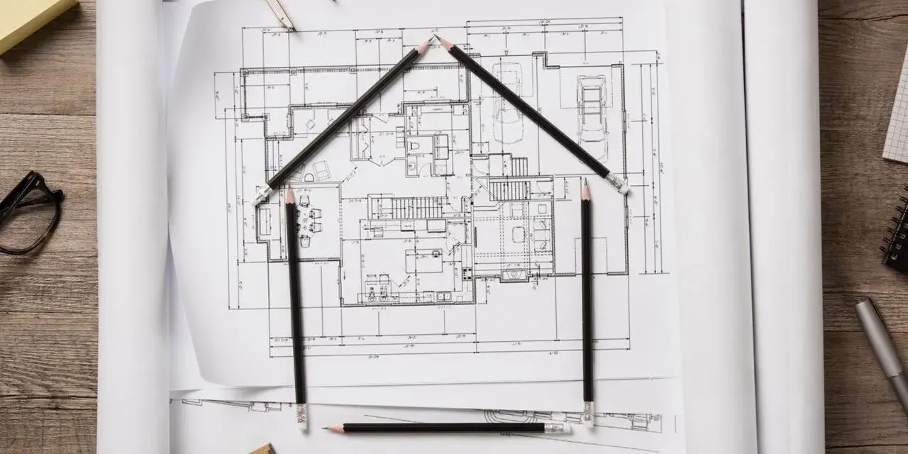 Architekt tworzy dom z ołówków na planach. Obok klucze i cyrkiel.