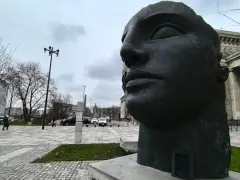 Duża, ciemna rzeźba głowy Igora Mitoraja na tle Teatru Dramatycznego w Warszawie.