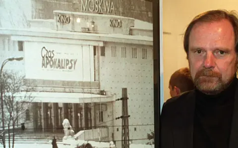 Mężczyzna z brodą obok plakatu kina "Moskwa" z napisem "Czas Apokalipsy".