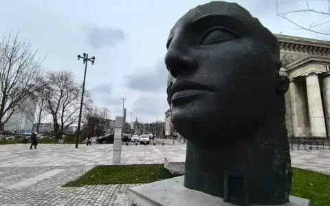 Duża, ciemna rzeźba głowy Igora Mitoraja na tle Teatru Dramatycznego w Warszawie.