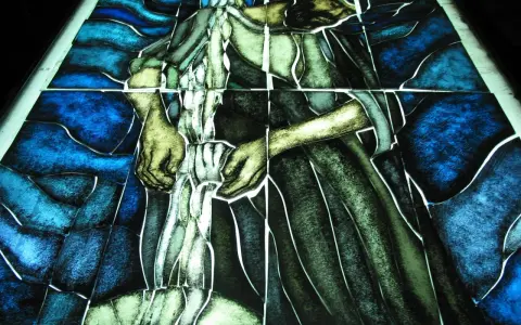 Fragment witrażu w stylu modernizm, przedstawiający postać w niebieskim i zielonym tle.