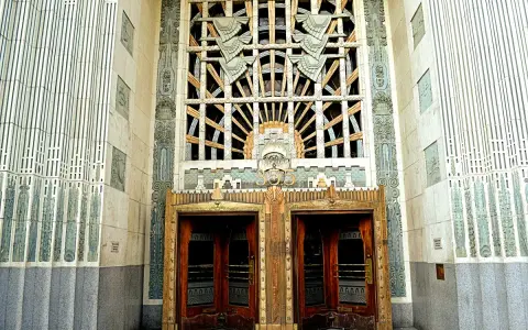 Monumentalne drzwi i okno w stylu art deco, ozdobione geometrycznymi wzorami i stylizowanymi motywami.