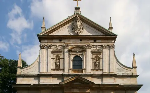 Bogata fasada kościoła w stylu barokowym, z rzeźbami i zdobieniami, pod błękitnym niebem.