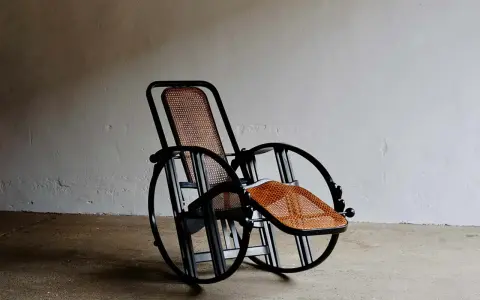 Huśtawka z plecionki, projekt Josefa Hoffmanna, z czarną metalową ramą i okrągłymi elementami.