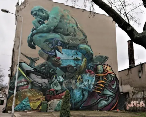 Co to jest mural? Ogromna, surrealistyczna grafika na ścianie budynku, przedstawiająca myślącą postać, krajobraz morski, jedzenie i przedmioty codziennego użytku.