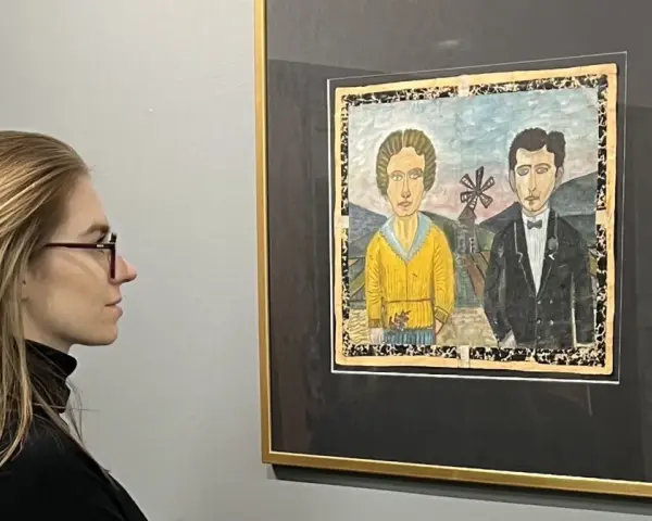 Kobieta w okularach podziwia obraz Nikifora z parą w strojach ślubnych. Czy to najdroższy obraz Nikifora?