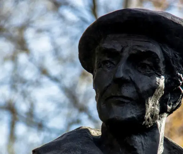 Portret rzeźbiarski w ciemnym brązie, ukazujący twarz mężczyzny w beretce. Widać głębokie zmarszczki i wyraziste rysy, oddające estetykę dzieł Kenara.