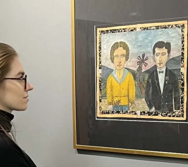 Kobieta w okularach podziwia obraz Nikifora z parą w strojach ślubnych. Czy to najdroższy obraz Nikifora?