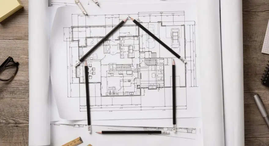 Architekt tworzy dom z ołówków na planach. Obok klucze i cyrkiel.