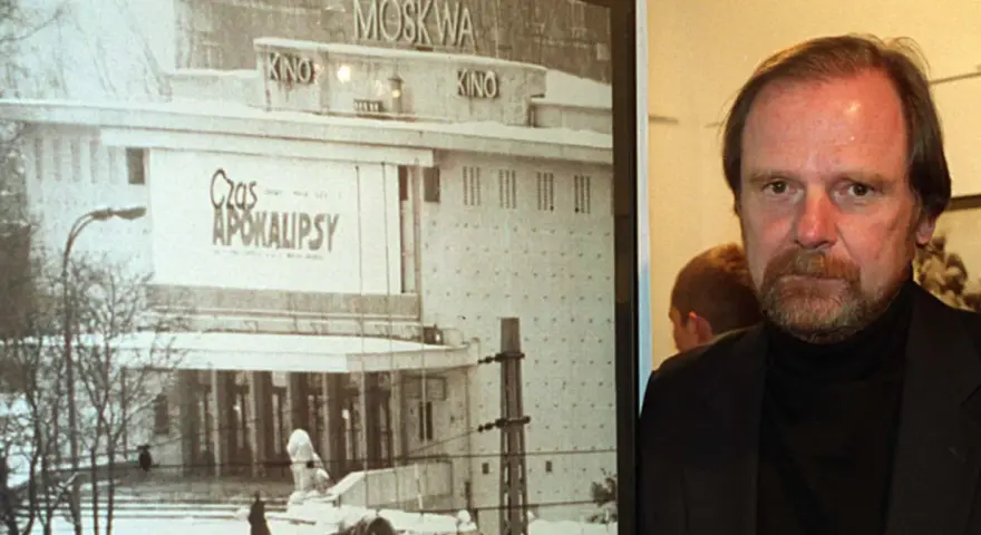 Mężczyzna z brodą obok plakatu kina "Moskwa" z napisem "Czas Apokalipsy".