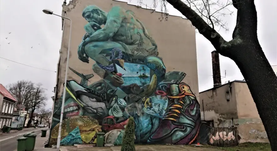 Co to jest mural? Ogromna, surrealistyczna grafika na ścianie budynku, przedstawiająca myślącą postać, krajobraz morski, jedzenie i przedmioty codziennego użytku.