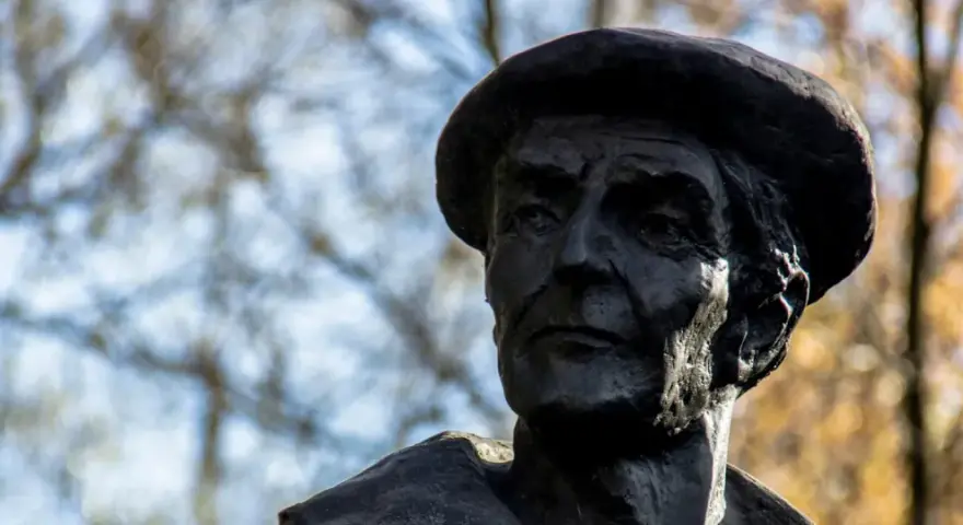 Portret rzeźbiarski w ciemnym brązie, ukazujący twarz mężczyzny w beretce. Widać głębokie zmarszczki i wyraziste rysy, oddające estetykę dzieł Kenara.