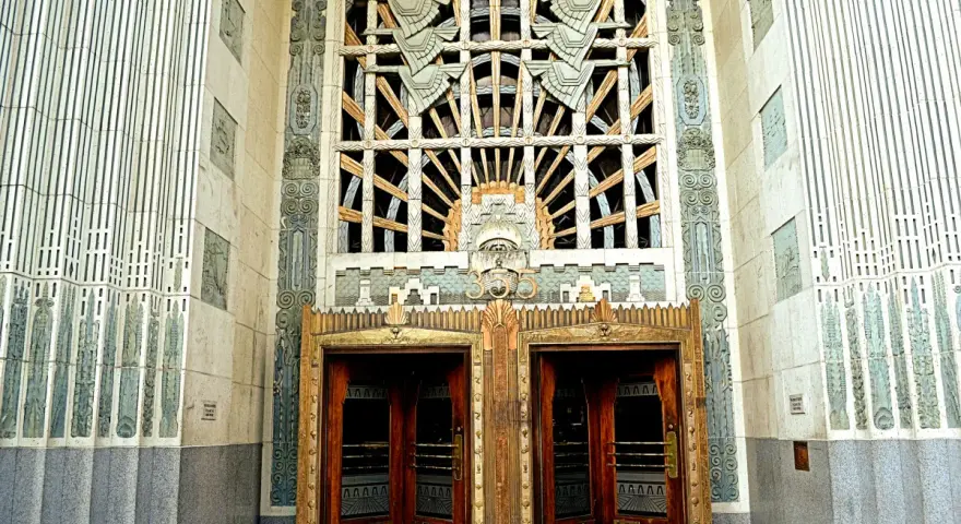 Monumentalne drzwi i okno w stylu art deco, ozdobione geometrycznymi wzorami i stylizowanymi motywami.