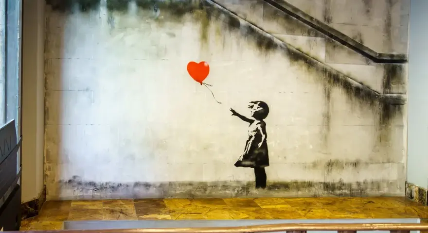 Banksy dziewczynka z balonikiem, unoszącym się na tle schodów i zniszczonej ściany.