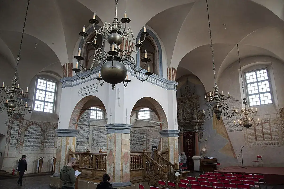Wnętrze zabytkowej synagogi w Polsce. Widać łukowate sklepienia, ozdobne żyrandole i hebrajskie napisy na ścianach.