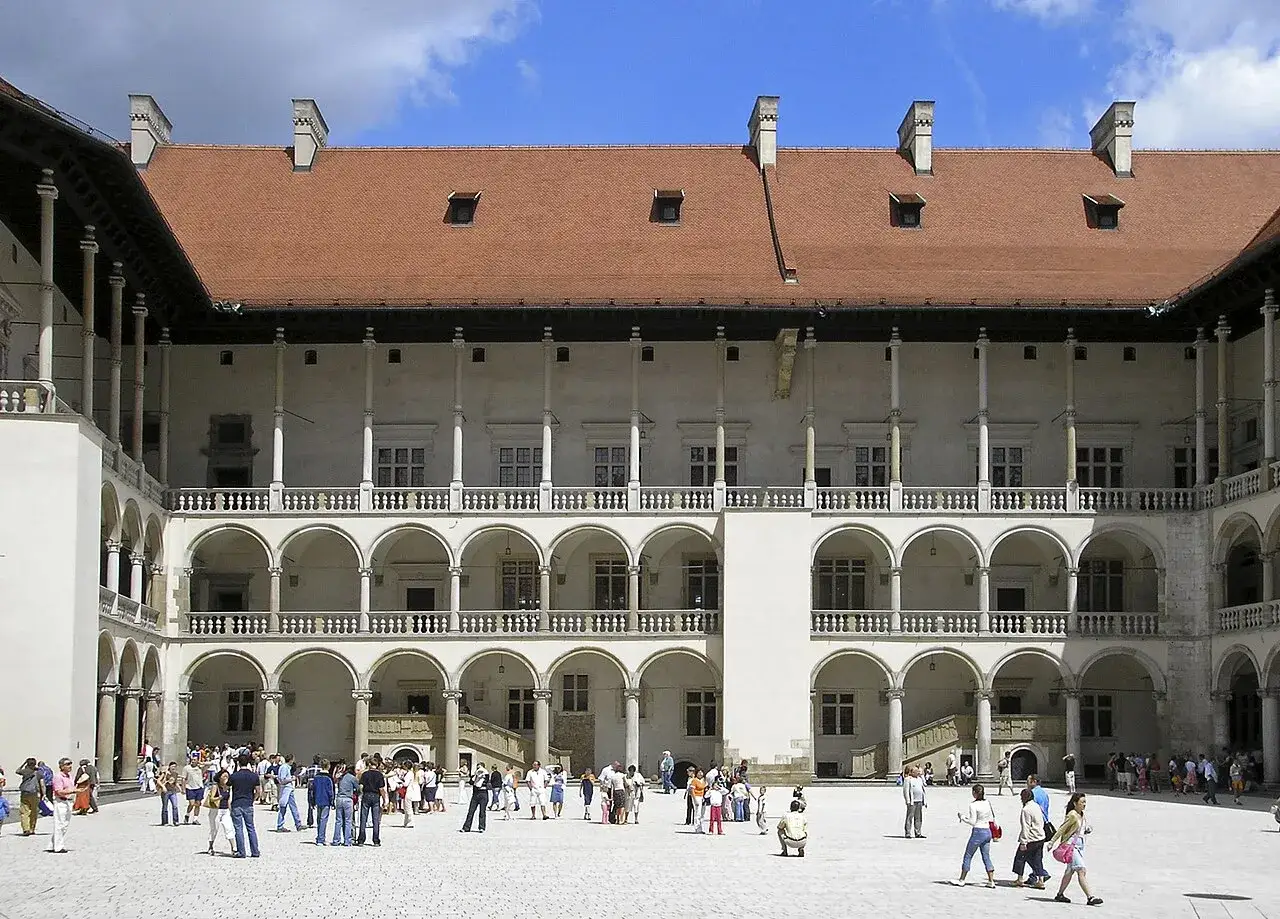 Dziedziniec zamku Wawel, arcydzieło polskiej architektury, z arkadowymi krużgankami i turystami spacerującymi po placu.