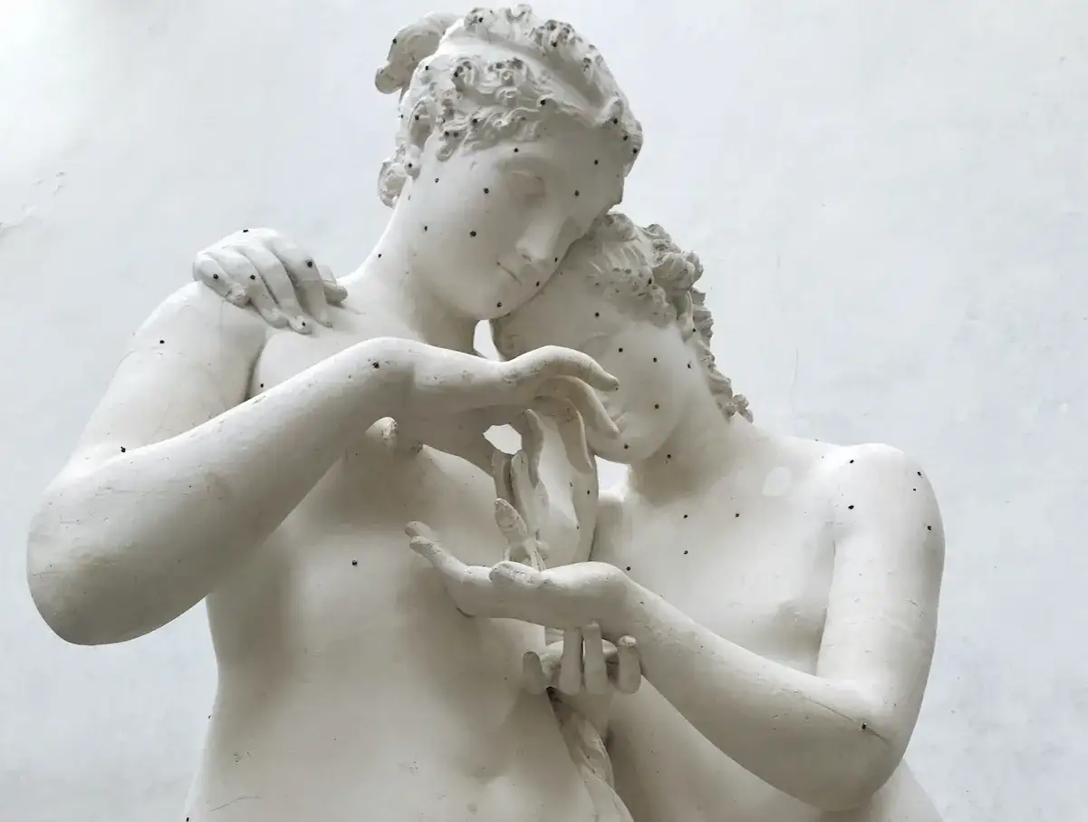 Biała rzeźba Amor i Psyche, ukazująca czułe objęcie i delikatny dotyk dłoni.